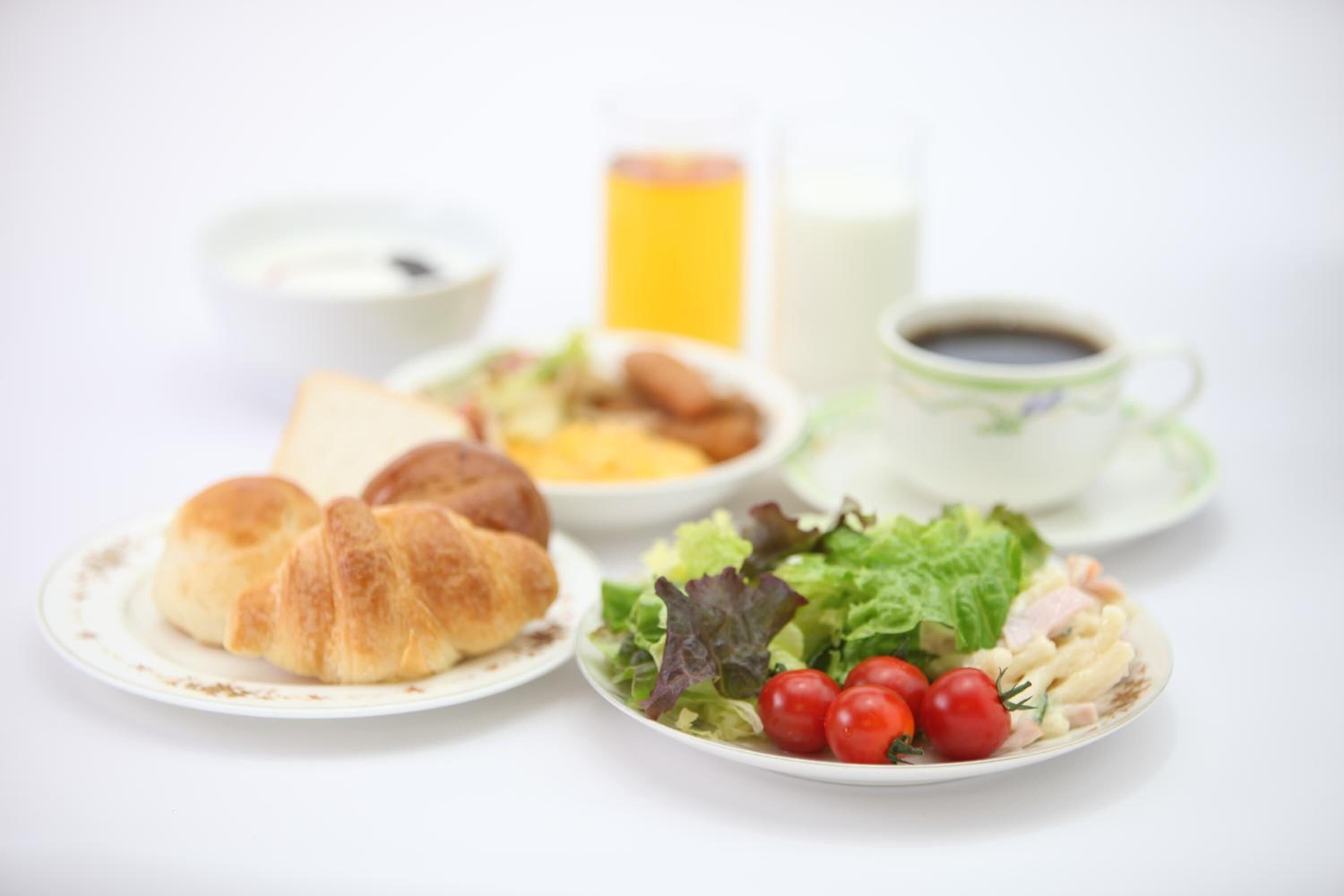 A breakfast setting with croissants, a salad, a bowl of soup, a glass of orange juice, and a cup of coffee.