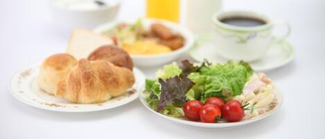 A breakfast setting with croissants, a salad, a bowl of soup, a glass of orange juice, and a cup of coffee.