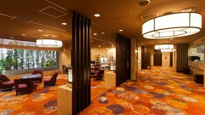 Een hotel lobby met een kamerbreed tapijt, een zithoek en grote ramen met uitzicht op bomen.