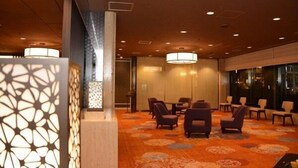 Een hotel lobby met een vloerbedekking, een zithoek met stoelen en tafels, en een decoratieve wand met een patroon.