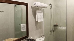 Casa de banho com cabine de chuveiro em vidro, sanita, lavatório e espelho.