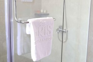 Mampara de ducha de vidrio con un perchero metálico sosteniendo una toalla blanca.