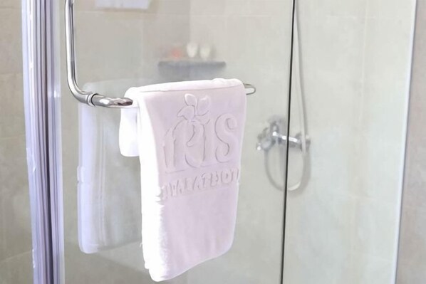 Lasiseinäinen suihkukaappi, jossa on metallinen pyyheteline ja sen päällä valkoinen pyyhe.