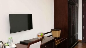 Quarto com televisão de tela plana na parede, escrivaninha de madeira com cesta, chaleira e uma xícara.