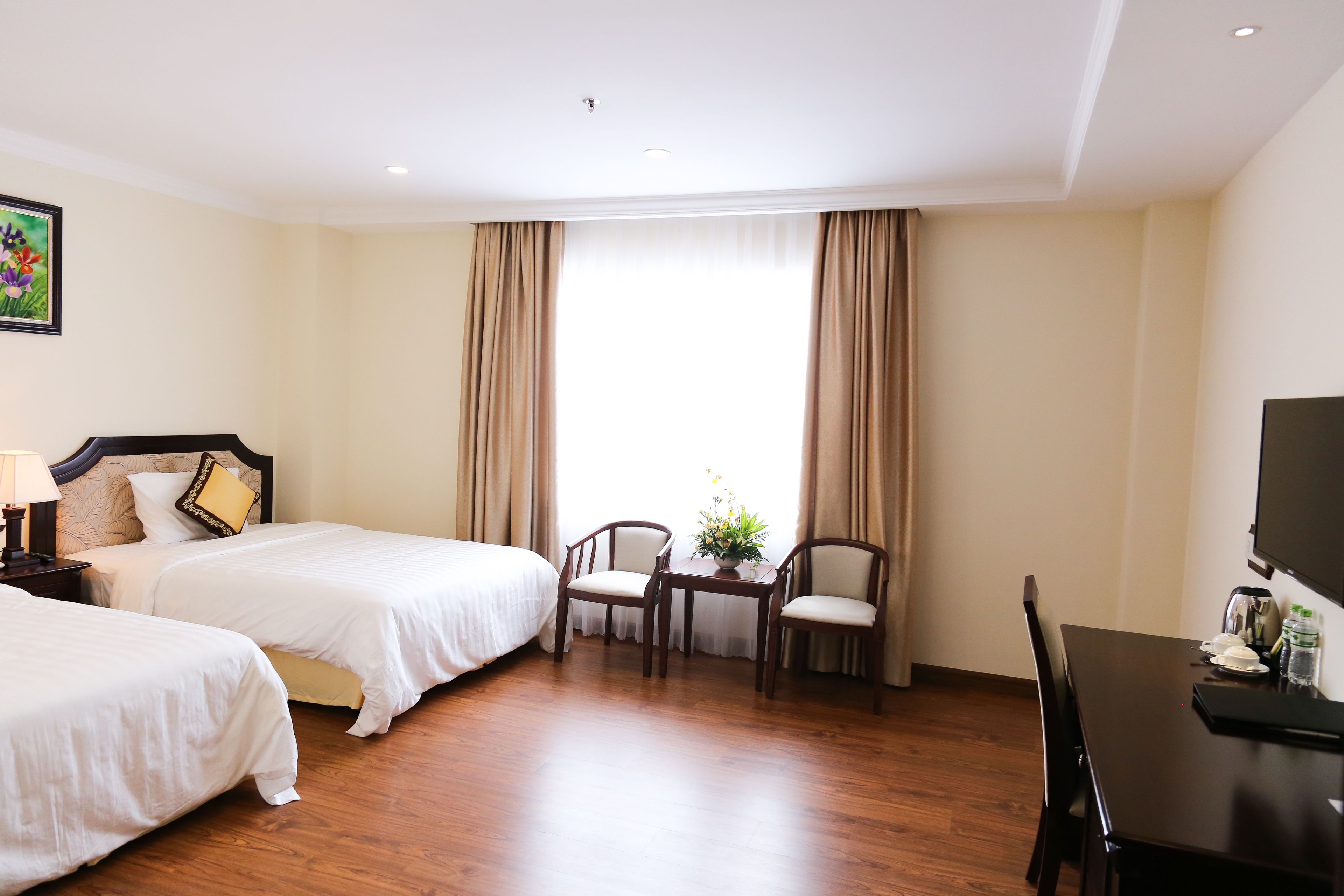 A hotel room with two beds, a dining table, chairs, a TV, and a window with curtains.