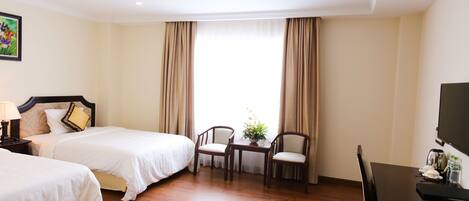 A hotel room with two beds, a dining table, chairs, a TV, and a window with curtains.