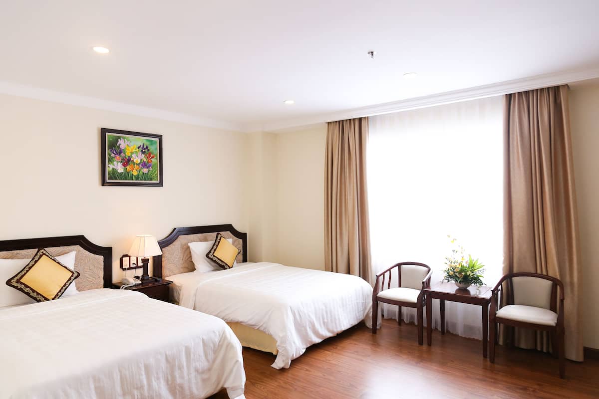 A hotel room with two beds, a nightstand, a chair, a table with a plant, and a painting on the wall.