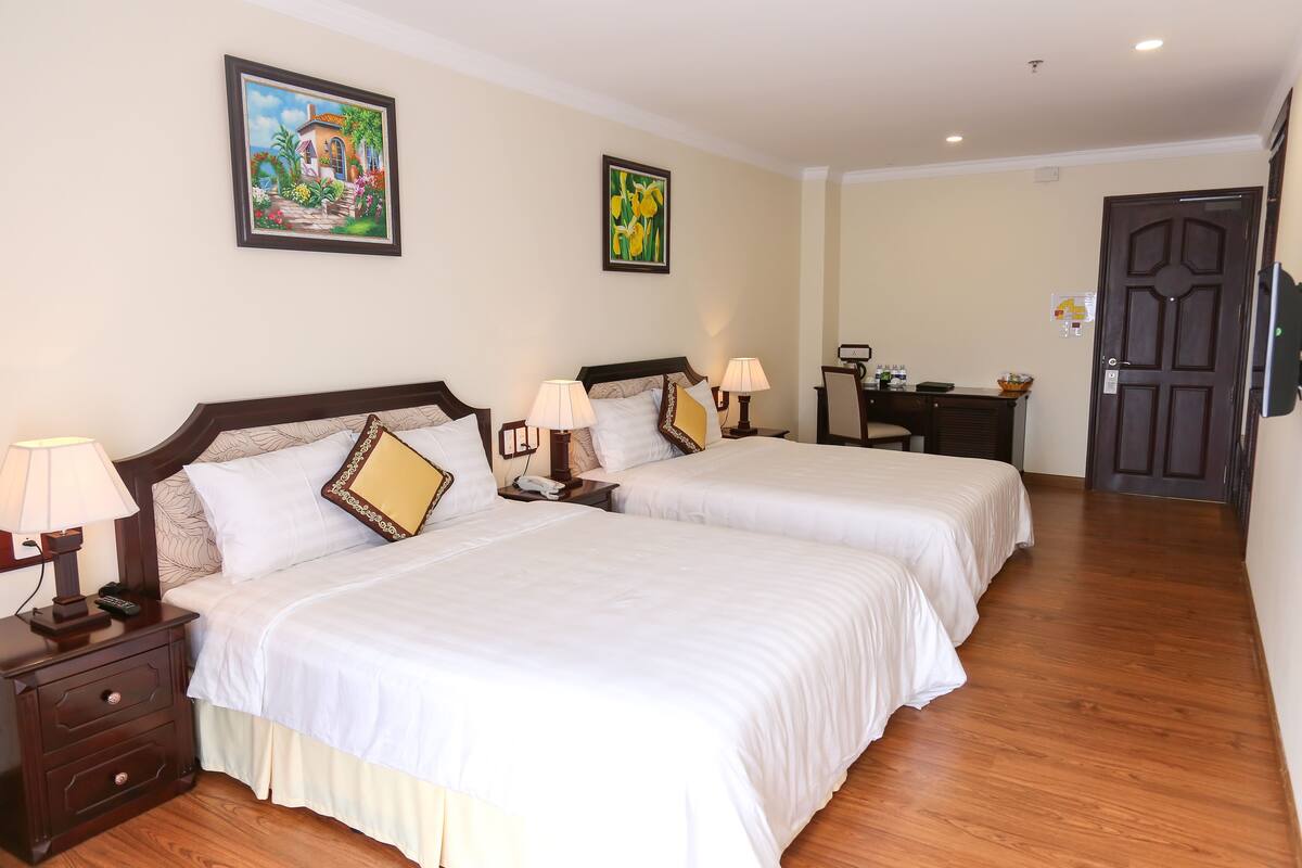 A hotel room with two beds, wooden flooring, and artwork on the walls.