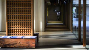 Un moderno vestíbulo de hotel con un mostrador de recepción de madera, una zona de estar con cojines y vistas amplias por grandes ventanales.