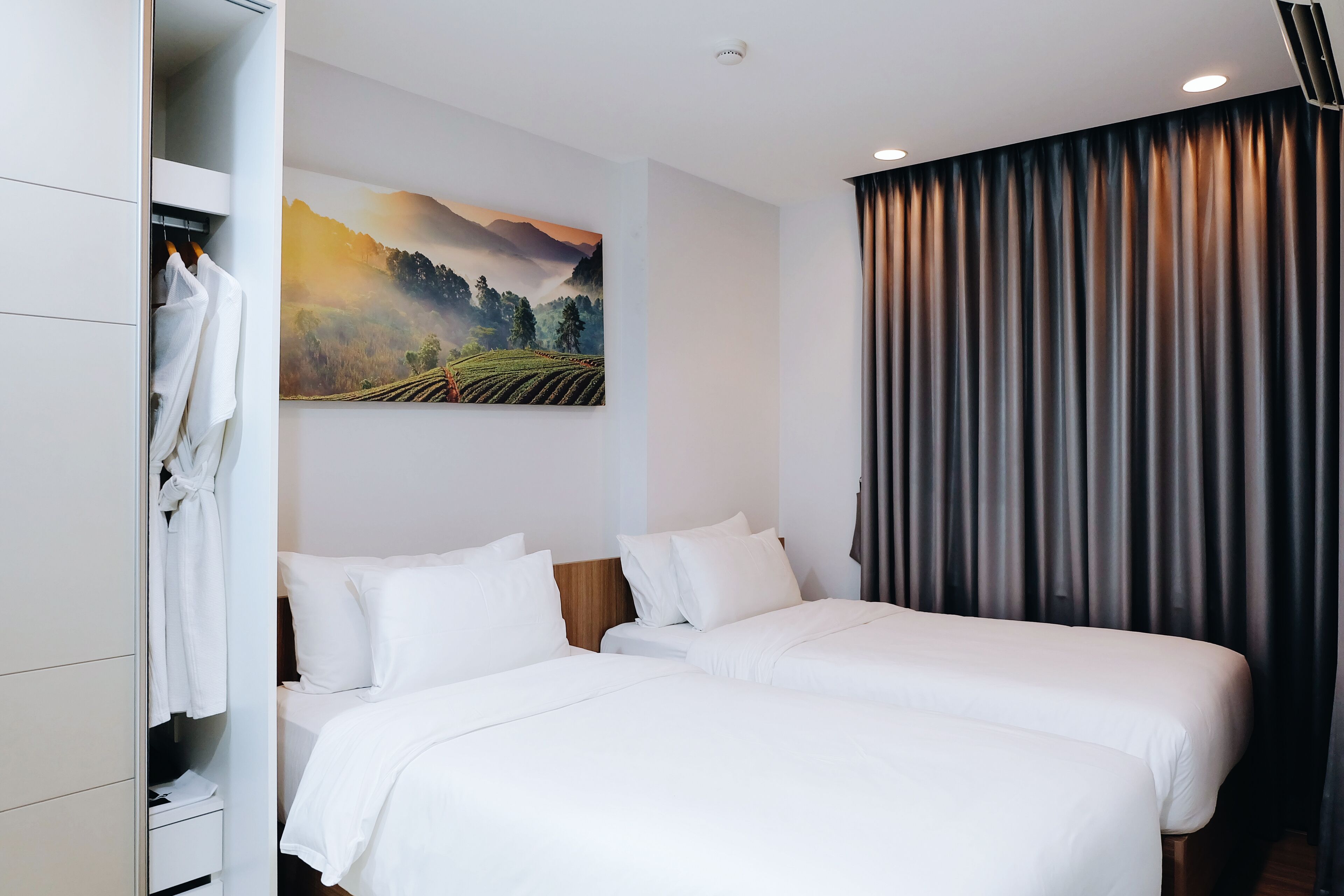 A hotel room with two beds, a wardrobe, a painting, and a curtain.