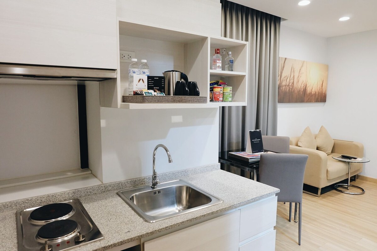 A modern kitchen with a built-in sink, a stove, and a countertop. There is a sofa and a small table in the adjacent living area.