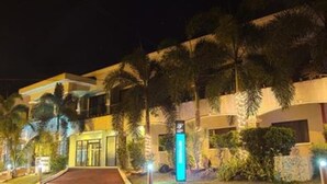 Un hotel de varios pisos, con palmeras y una entrada bien iluminada.