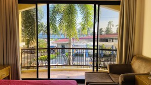 Una habitación con un gran ventanal, un balcón con barandilla de metal, un sofá marrón y una mesita.