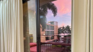 Vista desde un balcón con puerta de vidrio, que da a un edificio con alfombra roja y una palmera.
