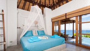 Un dormitorio con una cama grande, vista al mar y un balcón con barandilla de madera.