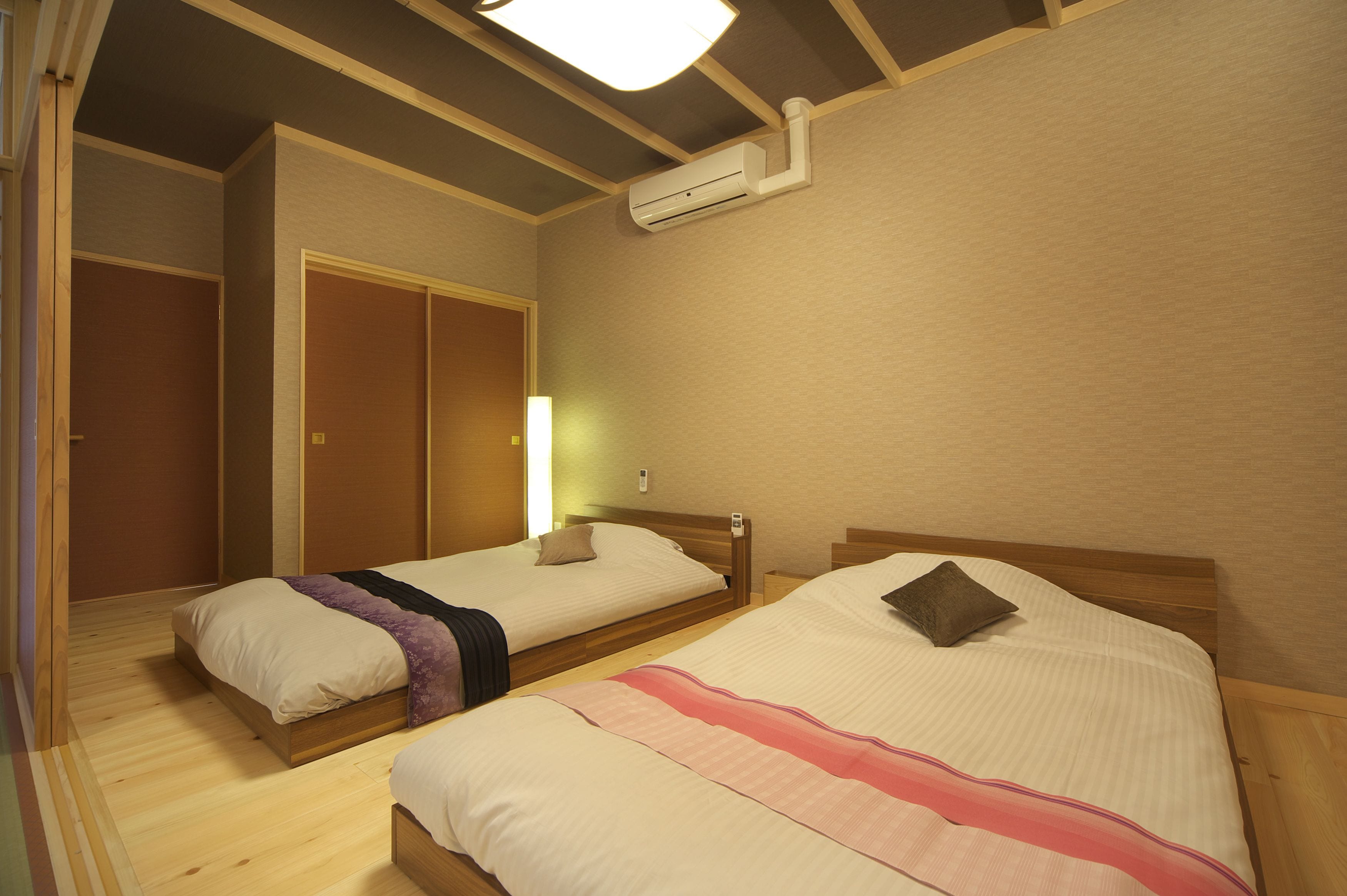 A room with two beds, wooden flooring, a ceiling fan, and an air conditioning unit.