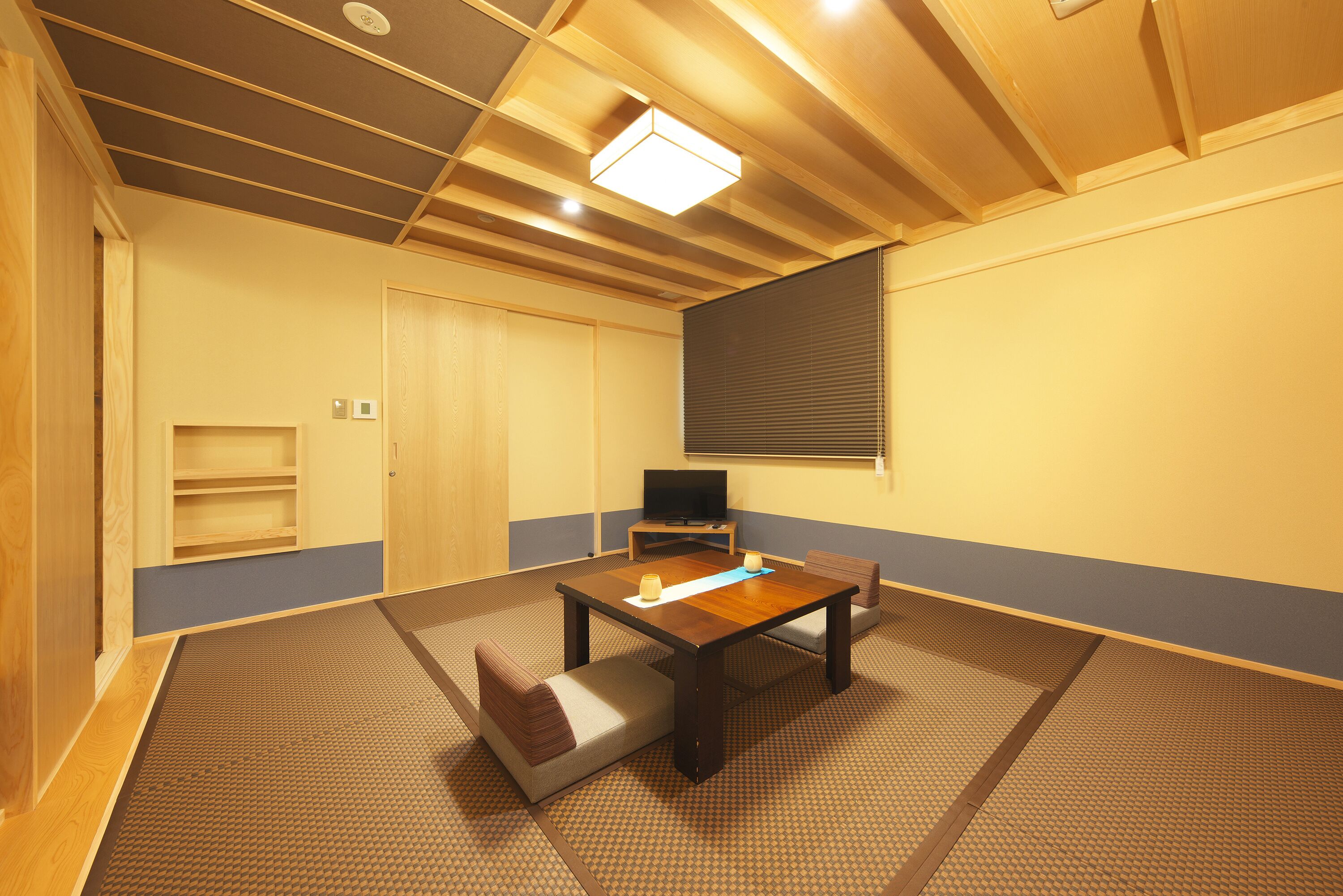 A room with tatami flooring, a low wooden table, two cushions, a television, and a sliding door.