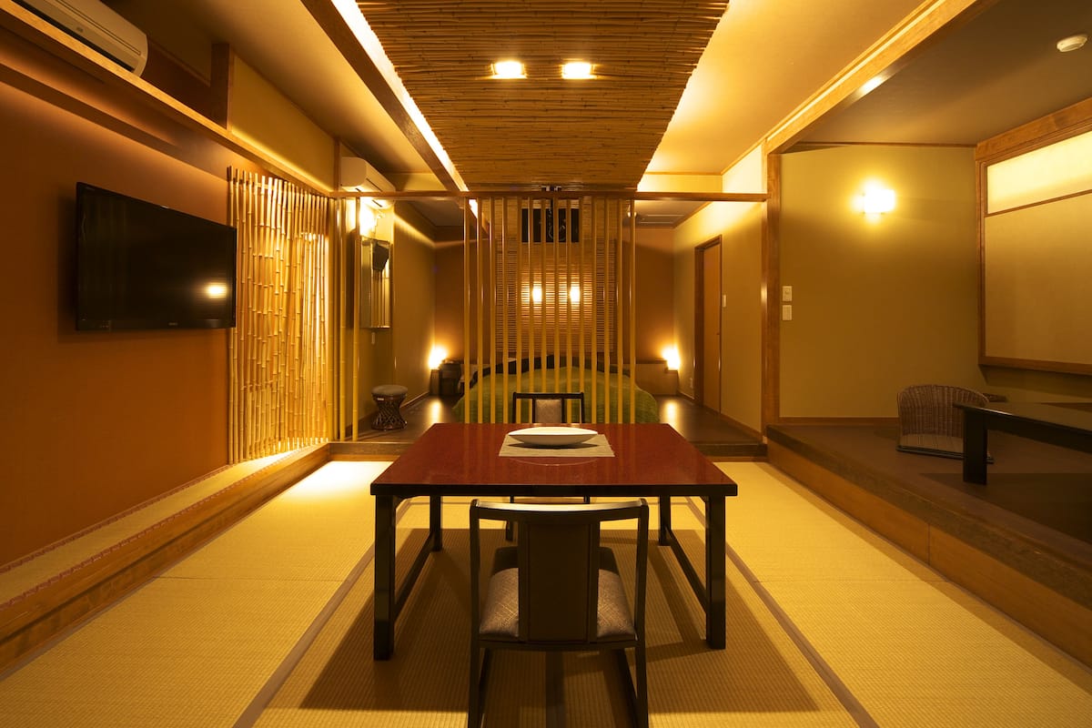 A traditional Japanese room with tatami flooring, a low wooden table, and a television mounted on the wall.