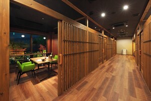 Un interior moderno con piso de madera, un área de comedor con sillas verdes y vistas a zonas verdes al exterior.