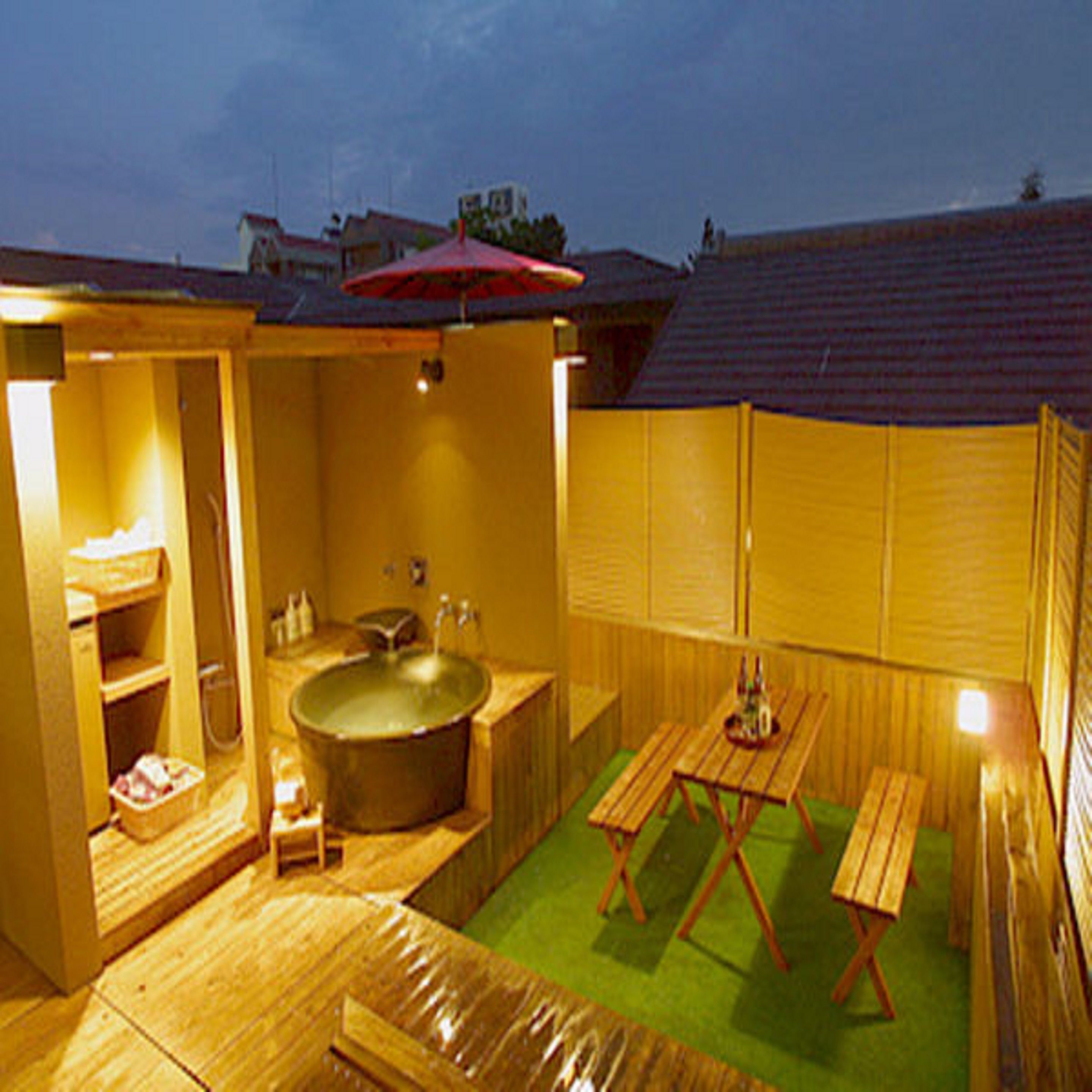 A wooden outdoor bathroom with a hot tub, wooden benches, and a small table.