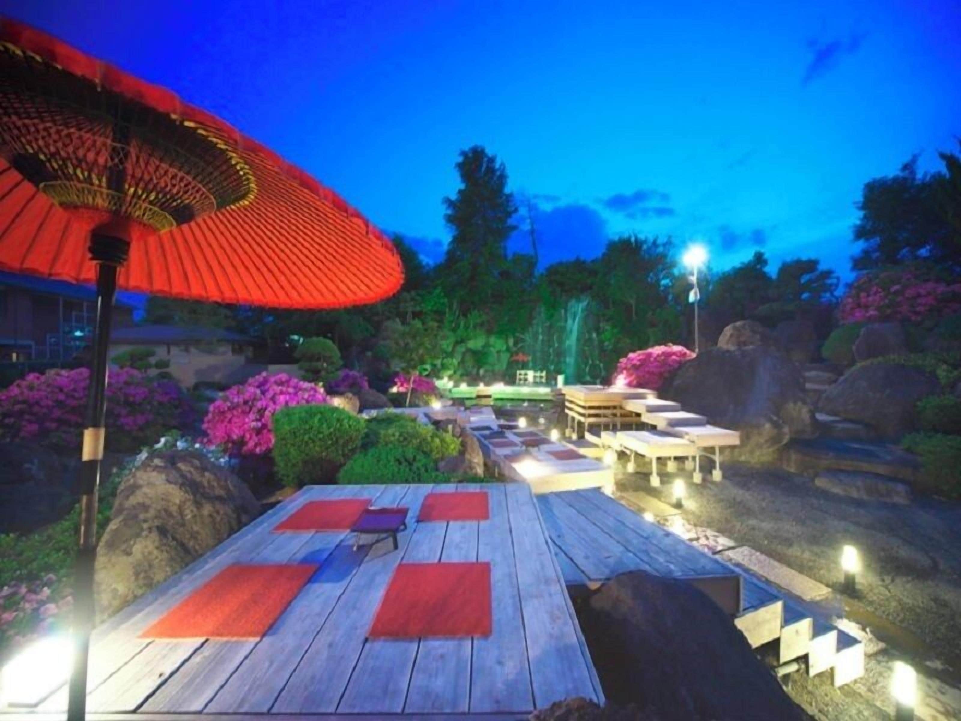 Un espace extérieur aménagé avec des tables et des bancs en bois, entouré de rochers et de plantes en fleurs.