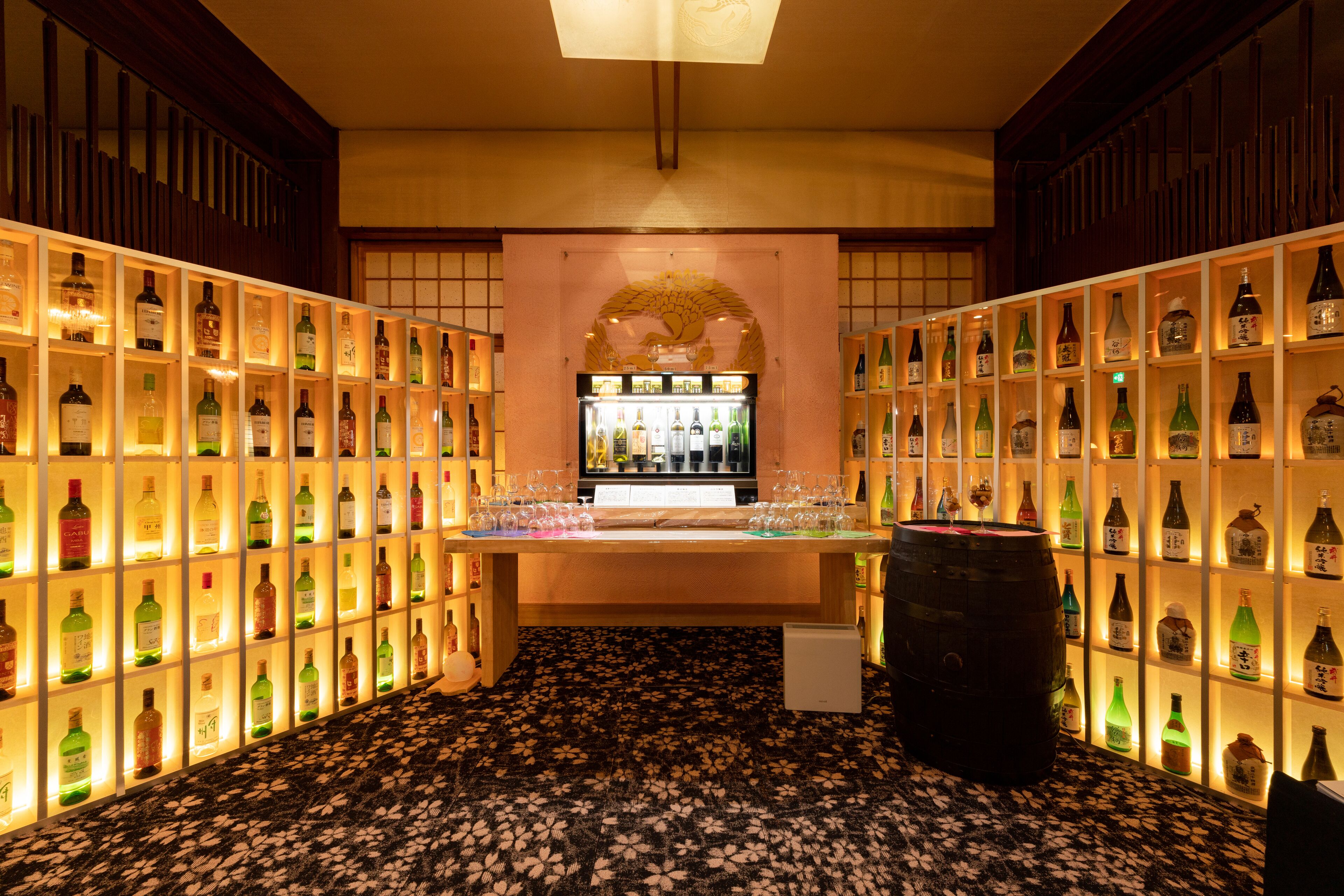A bar area with shelves of bottles and glasses, a wooden counter, and a patterned floor.