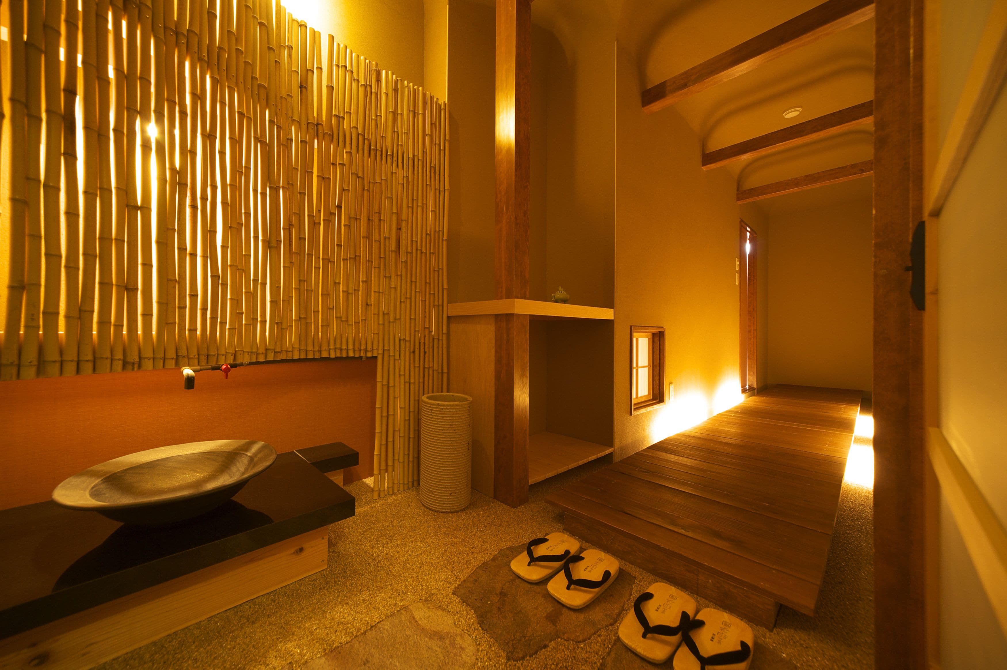 Une salle de spa avec un banc en bois, un petit lavabo et un mur en bambou.