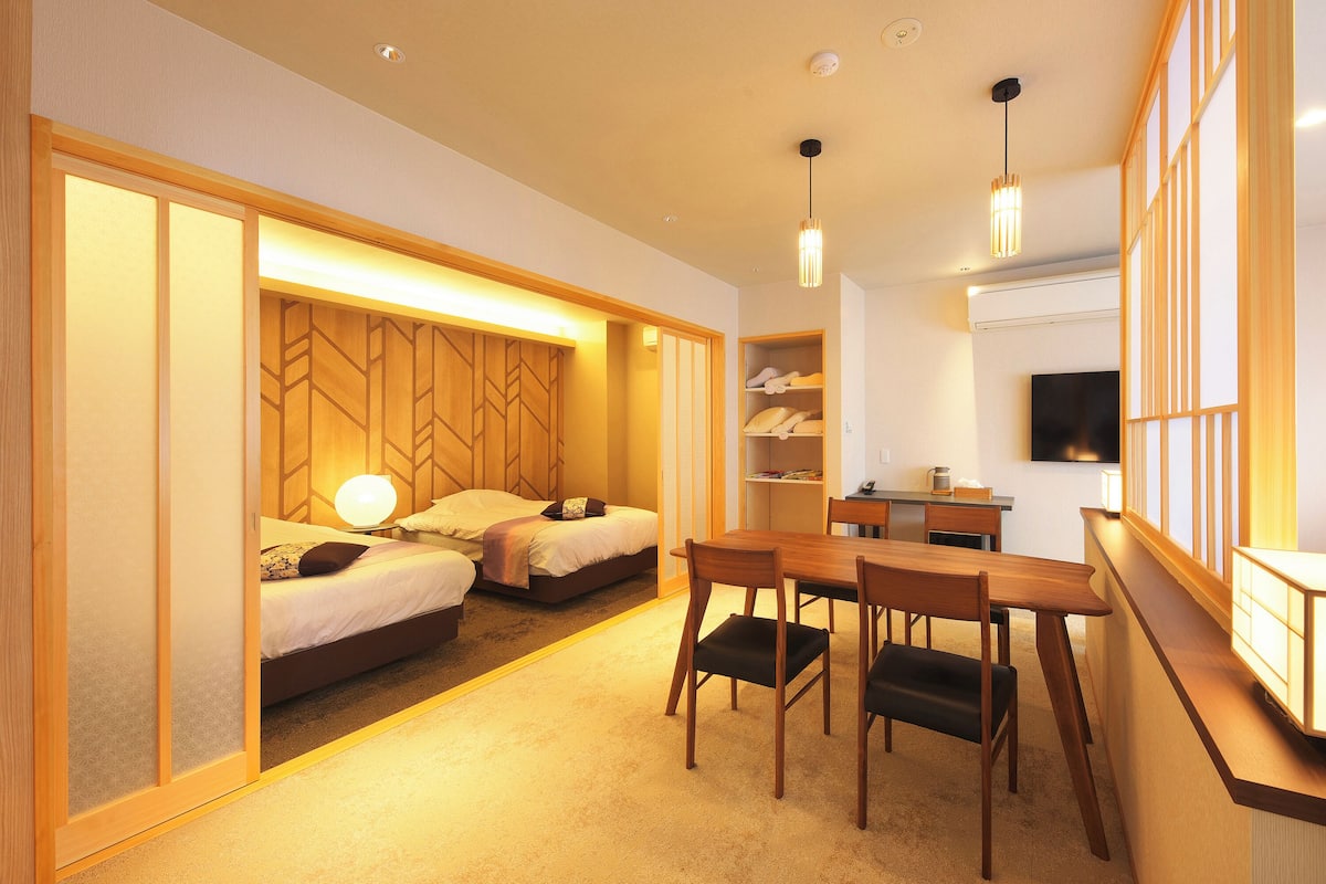 A hotel room with two beds, a dining area, and a TV.