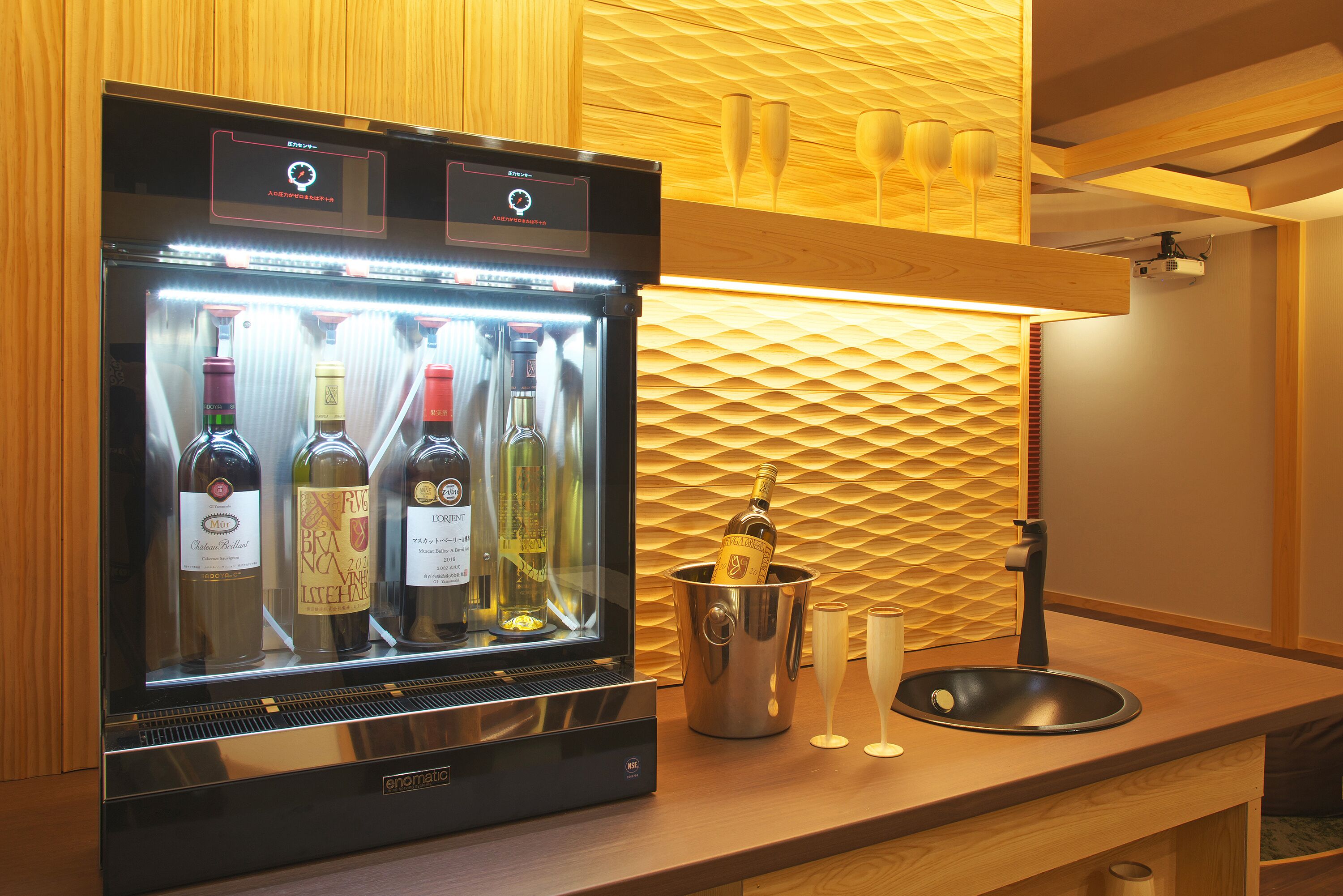 Mini-bar com refrigerador de vinhos, uma garrafa de champanhe e uma pia pequena.