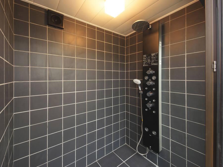 Una ducha moderna con panel de control, paredes de azulejos oscuros y una lámpara en el techo.