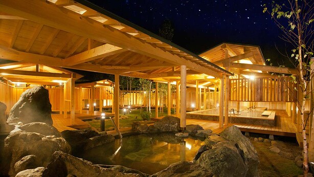 Un spa de madera con aguas termales, senderos de madera y un cielo nocturno.