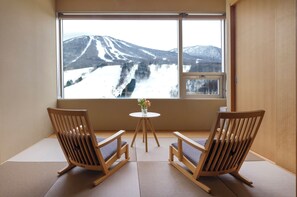 Habitació amb dues cadires de fusta orientades a una finestra gran amb vista a un paisatge de muntanya cobert de neu.