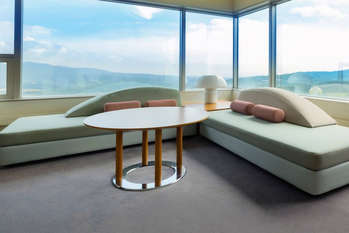 Una habitación moderna con un sofá modular, una mesa redonda y amplios ventanales con vistas al paisaje.