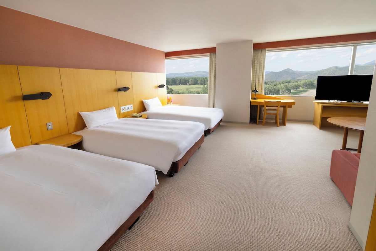 Habitación de hotel con tres camas, televisión, escritorio y vistas a las montañas.