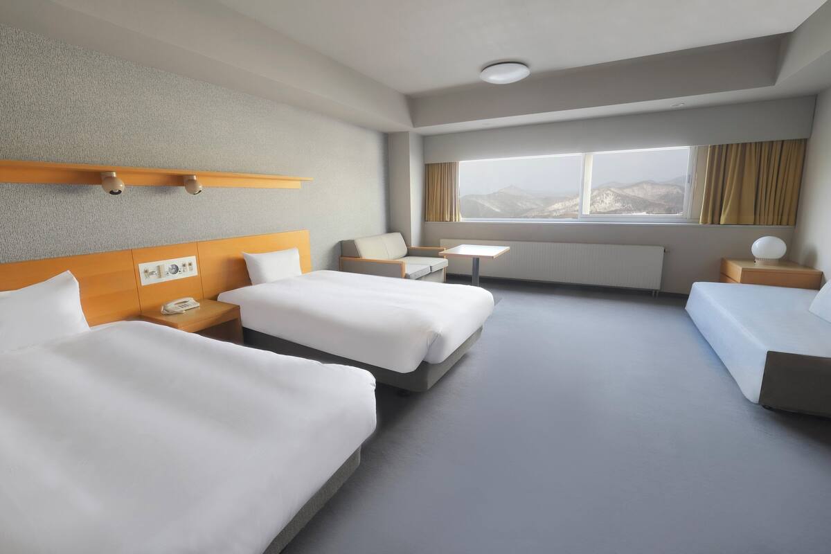 Habitación de hotel con dos camas, una mesita, una silla y ventana con vista a la montaña.