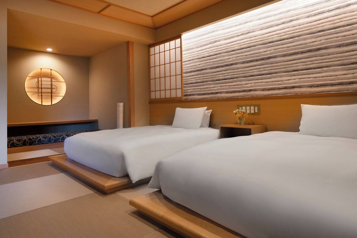 Habitación de hotel con dos camas, un tradicional panel japonés shoji y un aplique de pared.