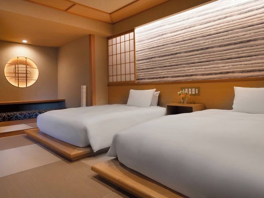 A hotel room with two beds, a traditional Japanese shoji screen, and a wall-mounted light fixture.