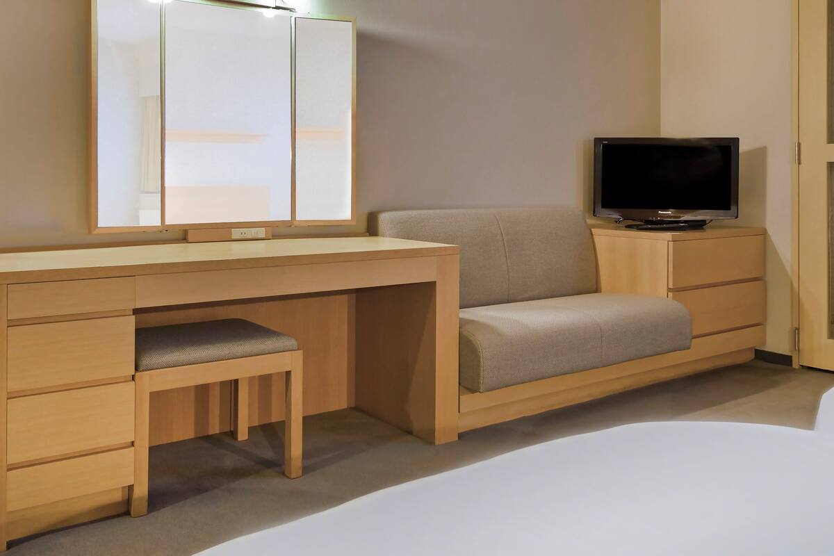 A hotel room with a wooden desk, a television, a sofa, and a wardrobe.