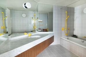 Un baño moderno con un espejo grande, dos lavamanos, una bañera y accesorios amarillos.