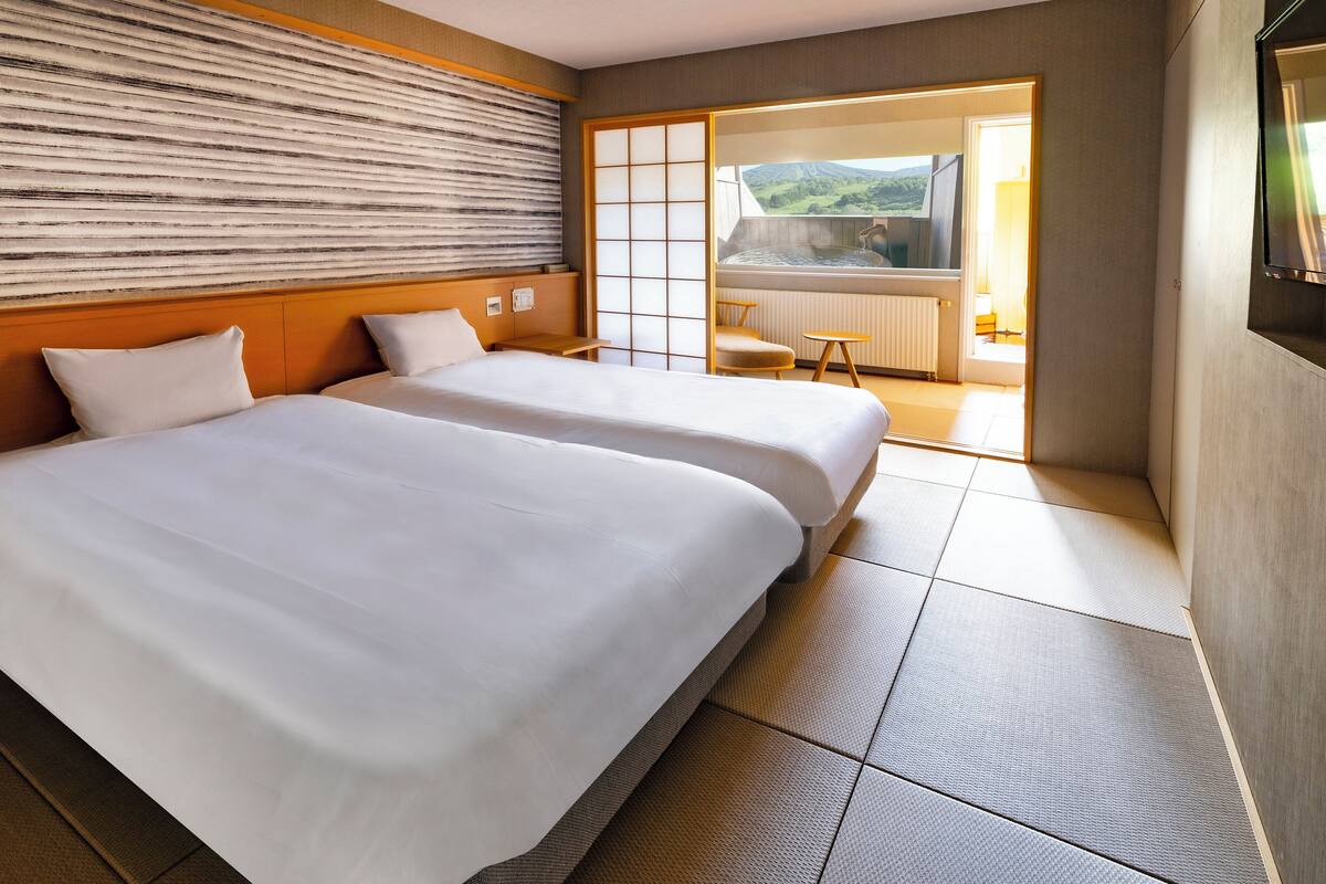Habitación de hotel con dos camas, vistas a un manantial termal y puerta corrediza a un balcón.