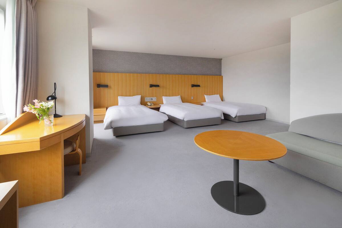 Una habitación de hotel con tres camas, un escritorio, una mesa redonda y un sofá.