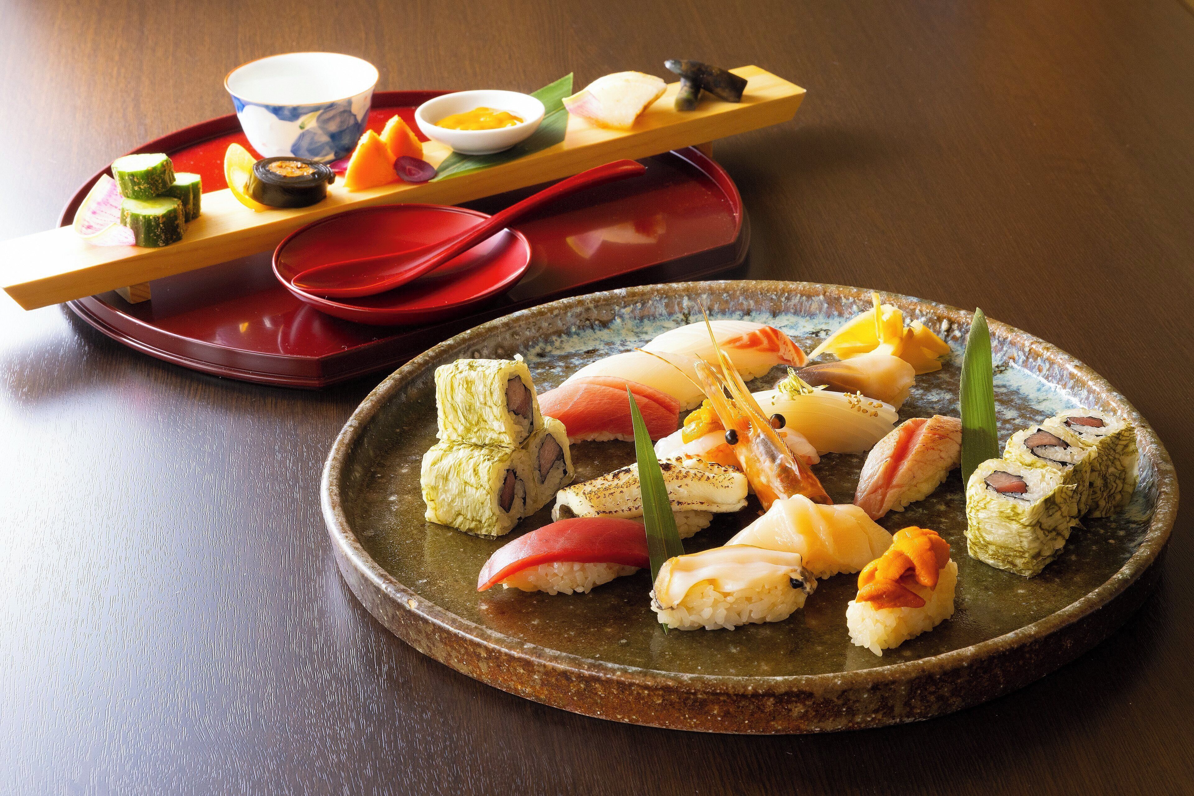 A sushi platter with various types of sushi and a small bowl of sauce on a ceramic plate.