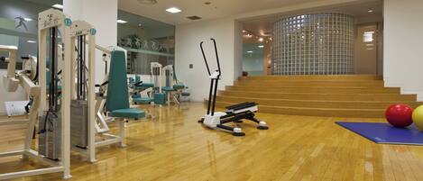 Un gimnasio con equipo de ejercicio, piso de madera y una escalera que sube a un nivel superior.