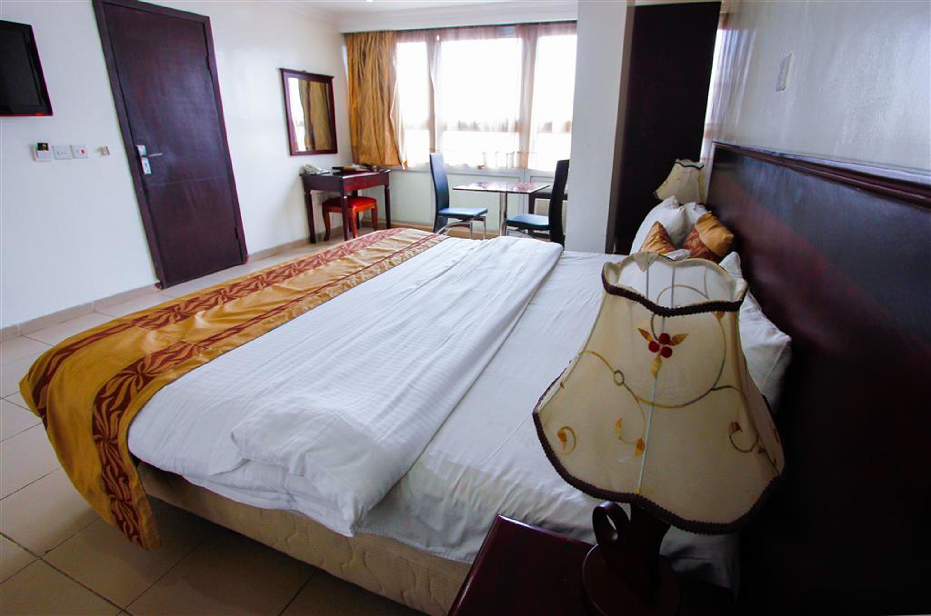 Une chambre d’hôtel avec un grand lit, un bureau, une chaise et une fenêtre avec des rideaux.