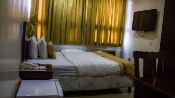 A hotel room with a bed, a TV mounted on the wall, a wooden chair, and a desk with a telephone.