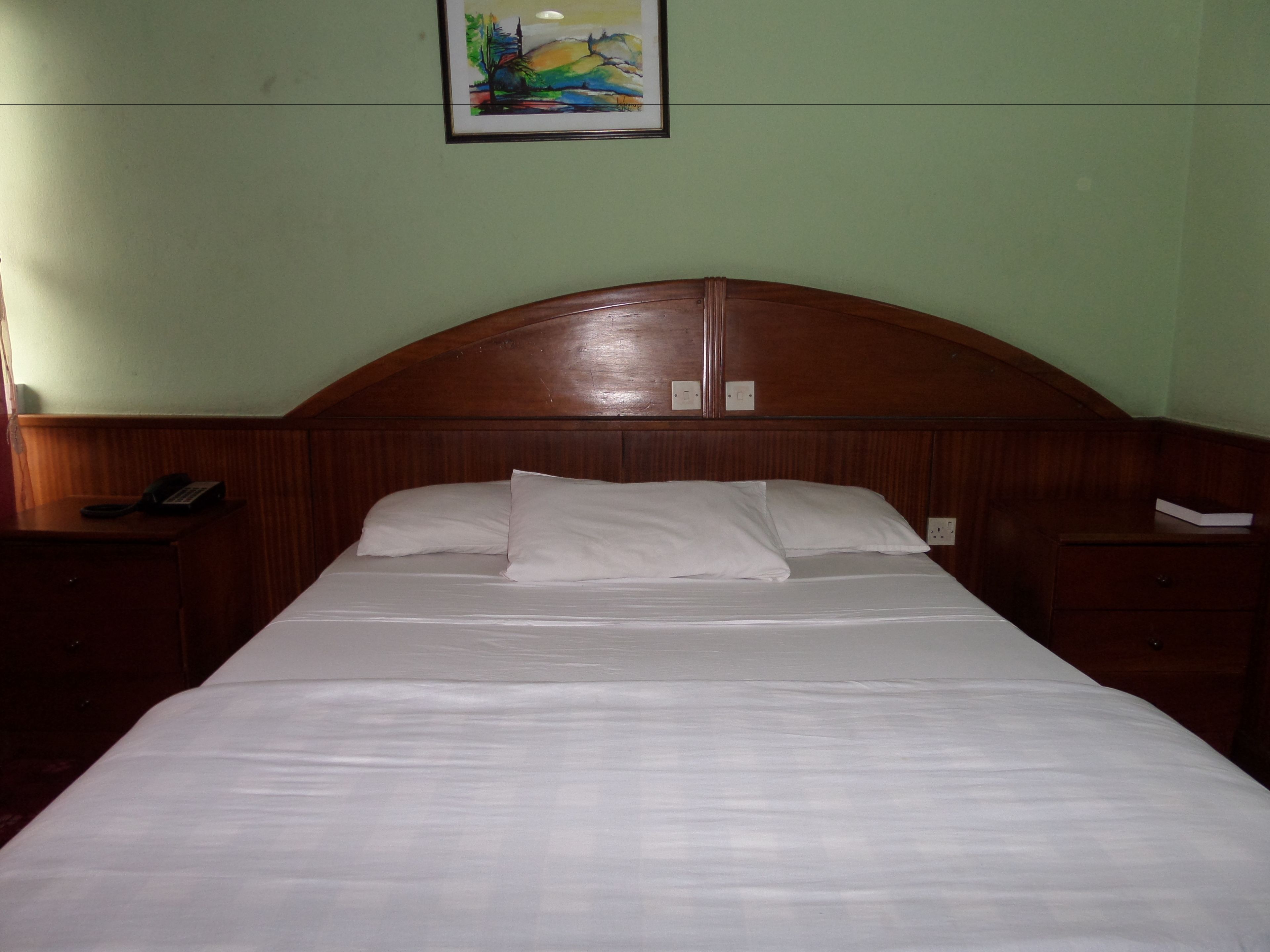 A neatly made bed in a room with a wooden headboard and a nightstand on the left.