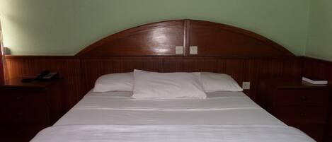A neatly made bed in a room with a wooden headboard and a nightstand on the left.