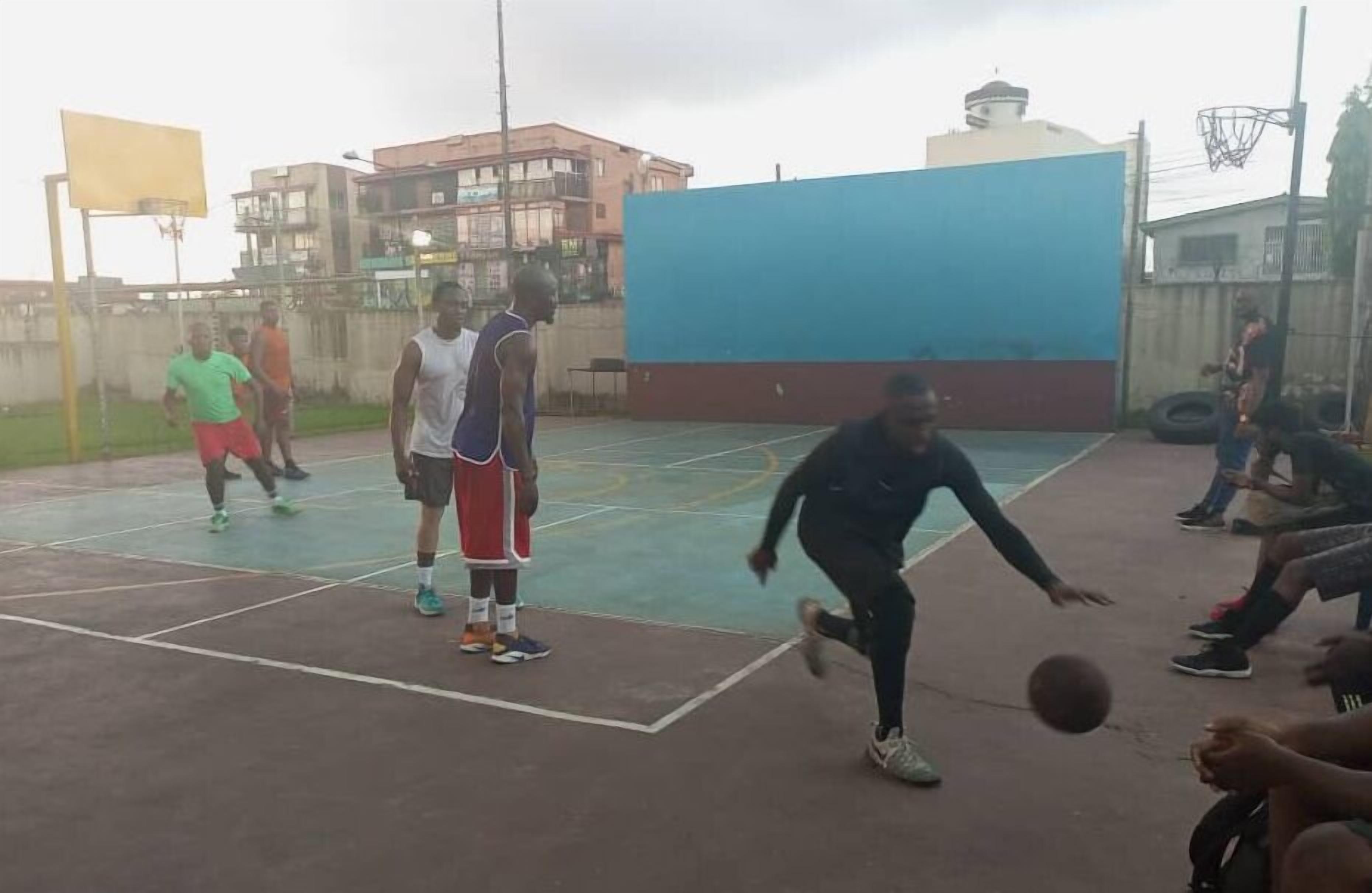 Una cancha de baloncesto al aire libre con superficie azul y roja, rodeada de edificios y un cielo despejado.