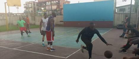 Una cancha de baloncesto al aire libre con superficie azul y roja, rodeada de edificios y un cielo despejado.
