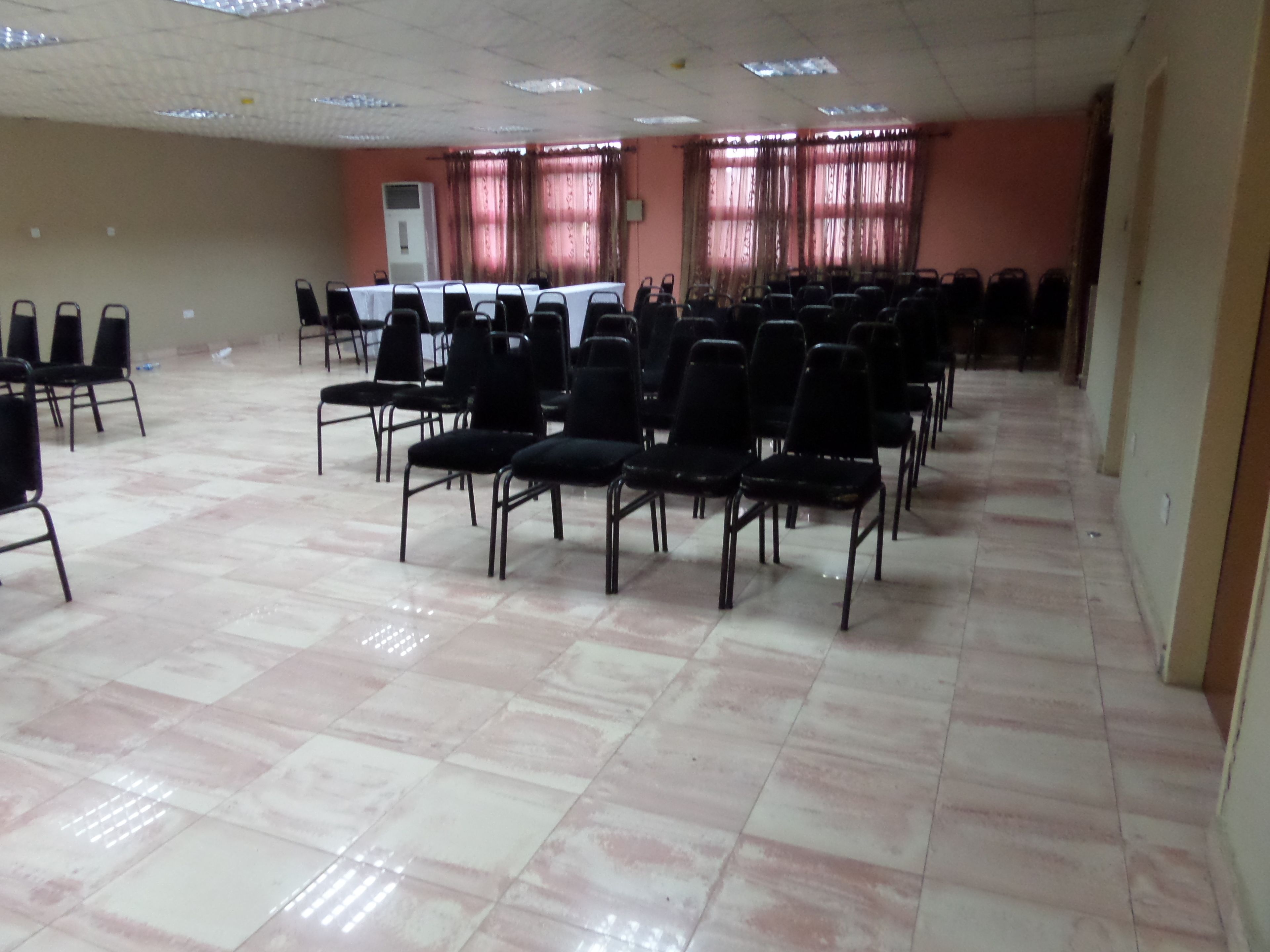 A conference room with rows of chairs, a long table, and a tiled floor.
